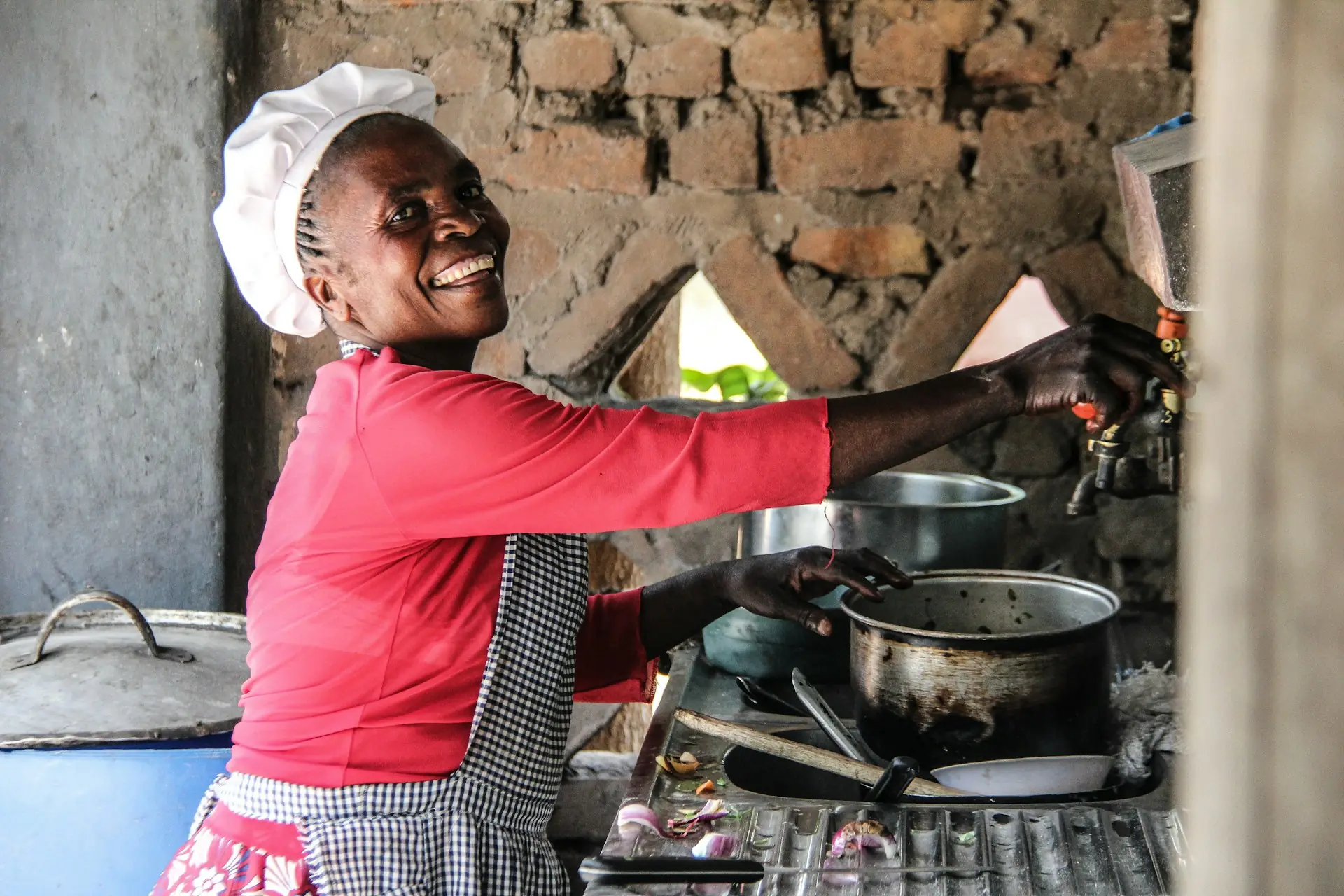 Naledi, nutritionist, laughing over her pots in a stone kitchen.