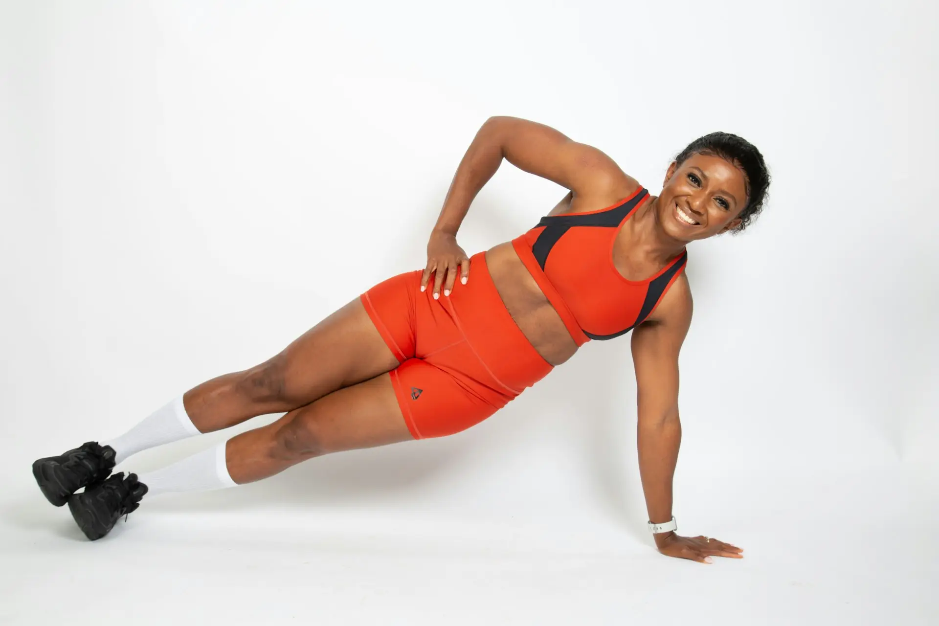 A woman in red holding a side plank, smiling through it.