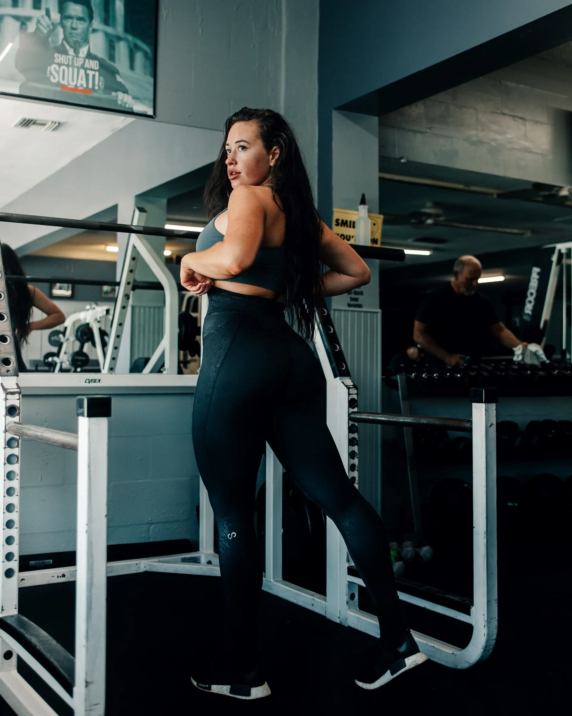 A woman at the squat rack, set square to the bar, seen from behind.
