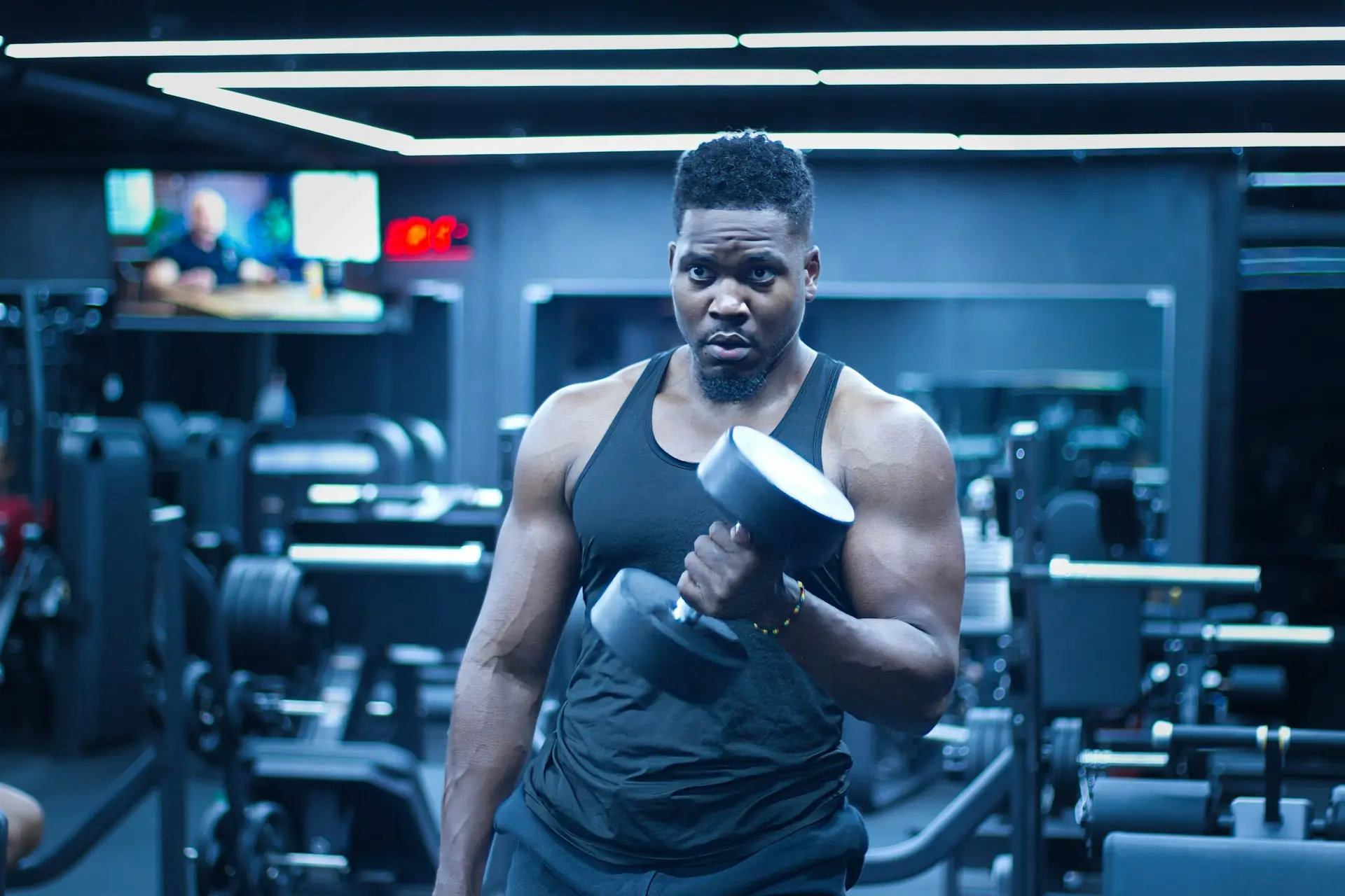 A man mid-curl with a heavy dumbbell in a dark gym.