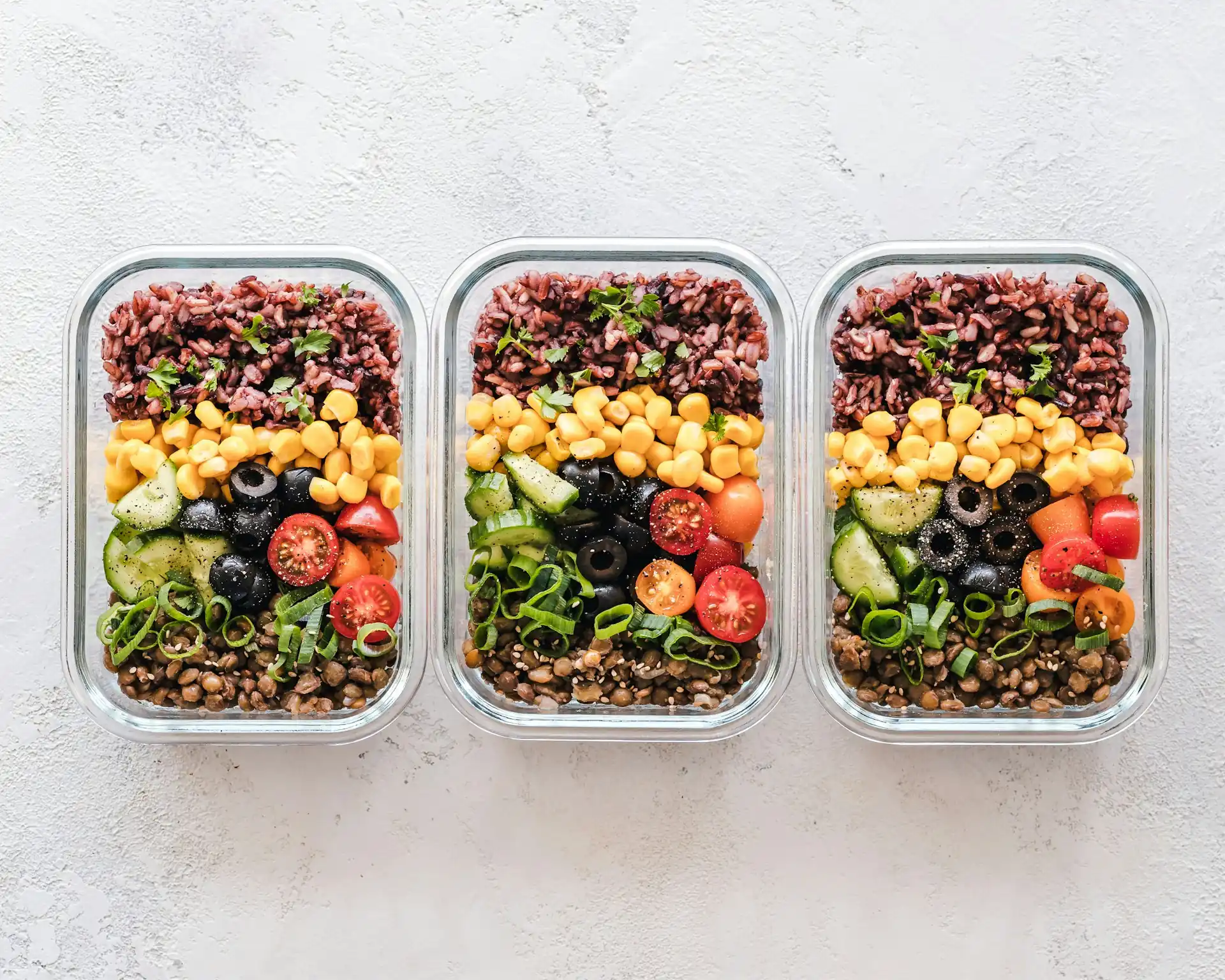 Three glass containers of prepped meals, bright with vegetables.
