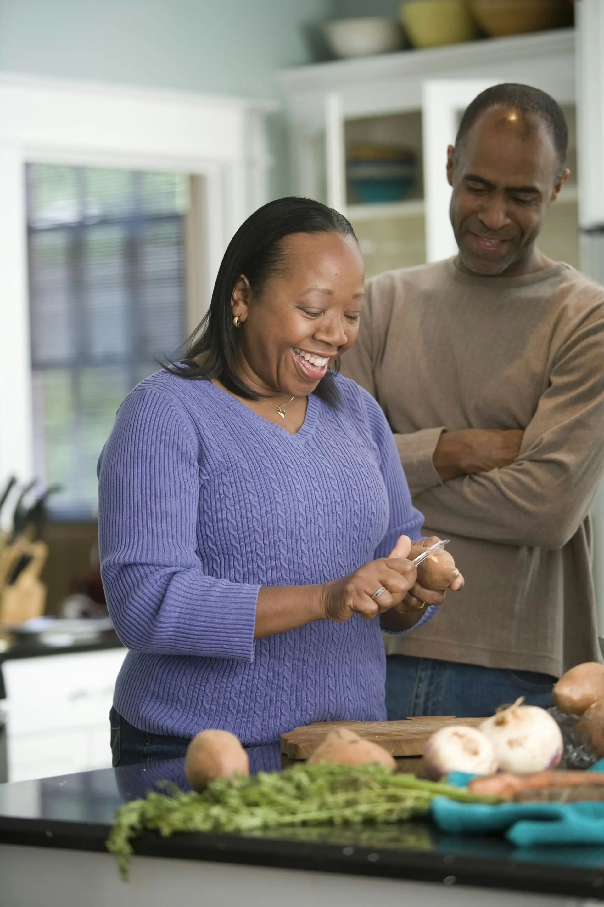 A couple laughing while prepping vegetables at their kitchen counter.