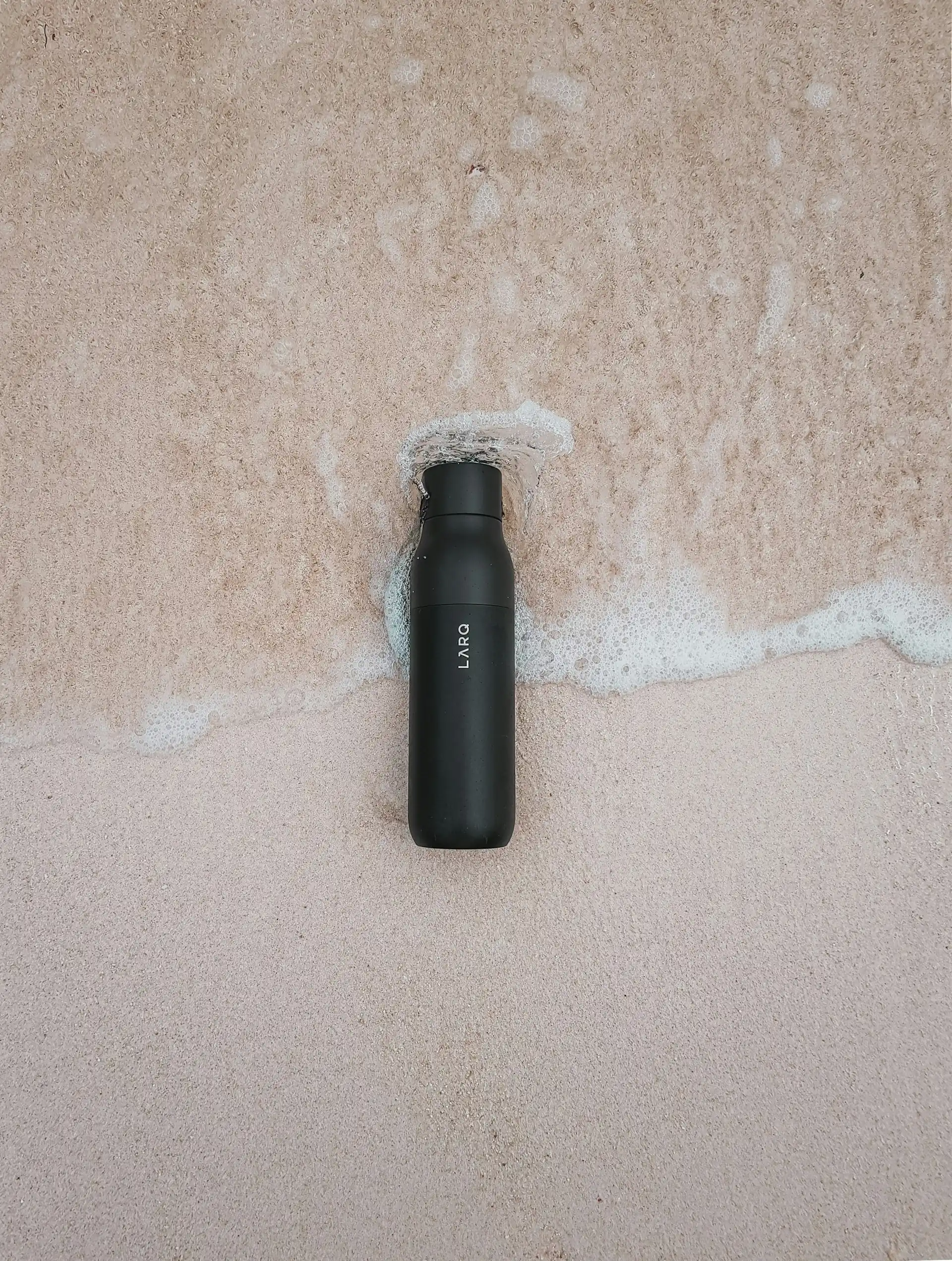 A black sports bottle at the shoreline.