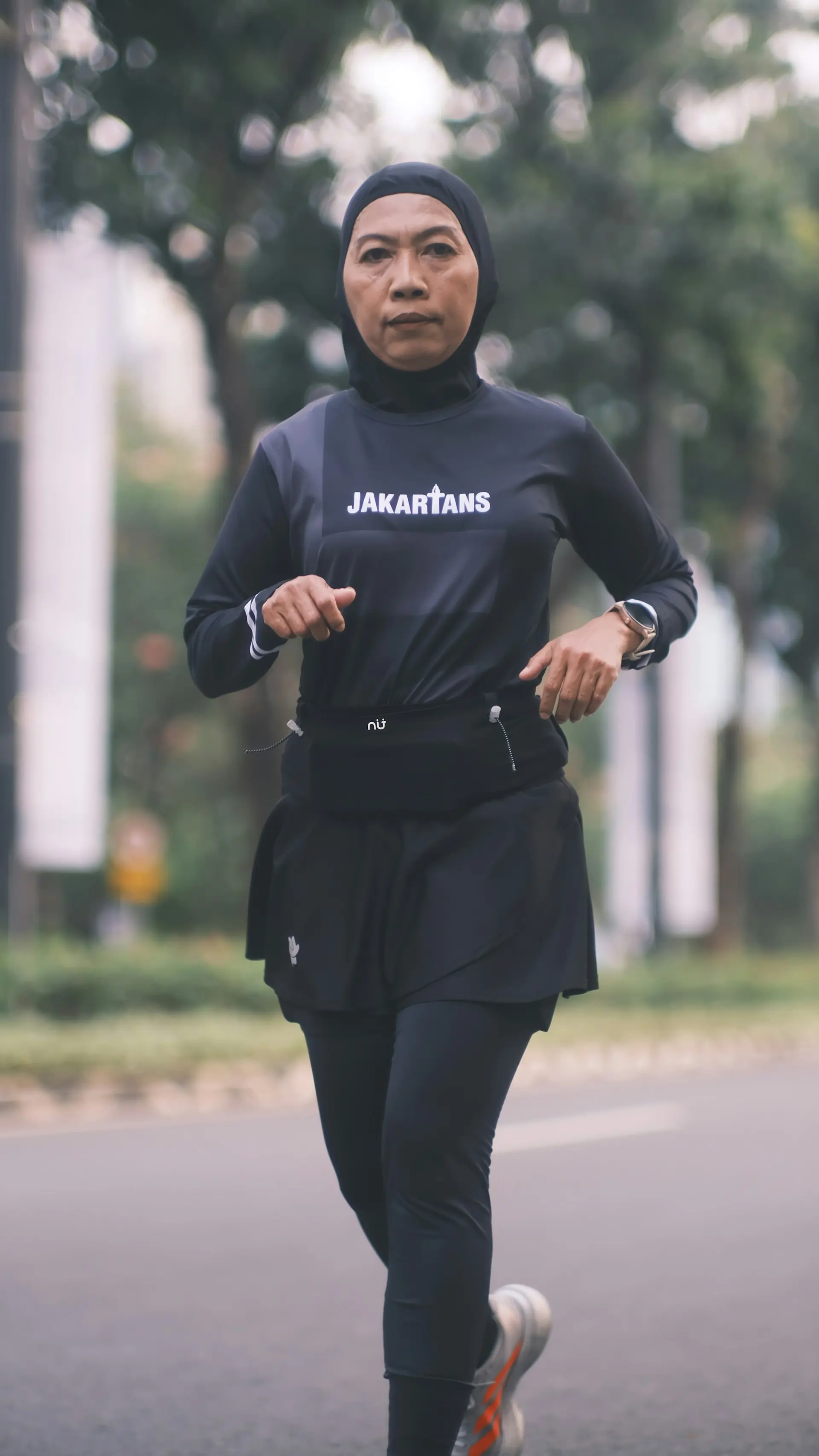 A woman in a black sport hijab running in the city.