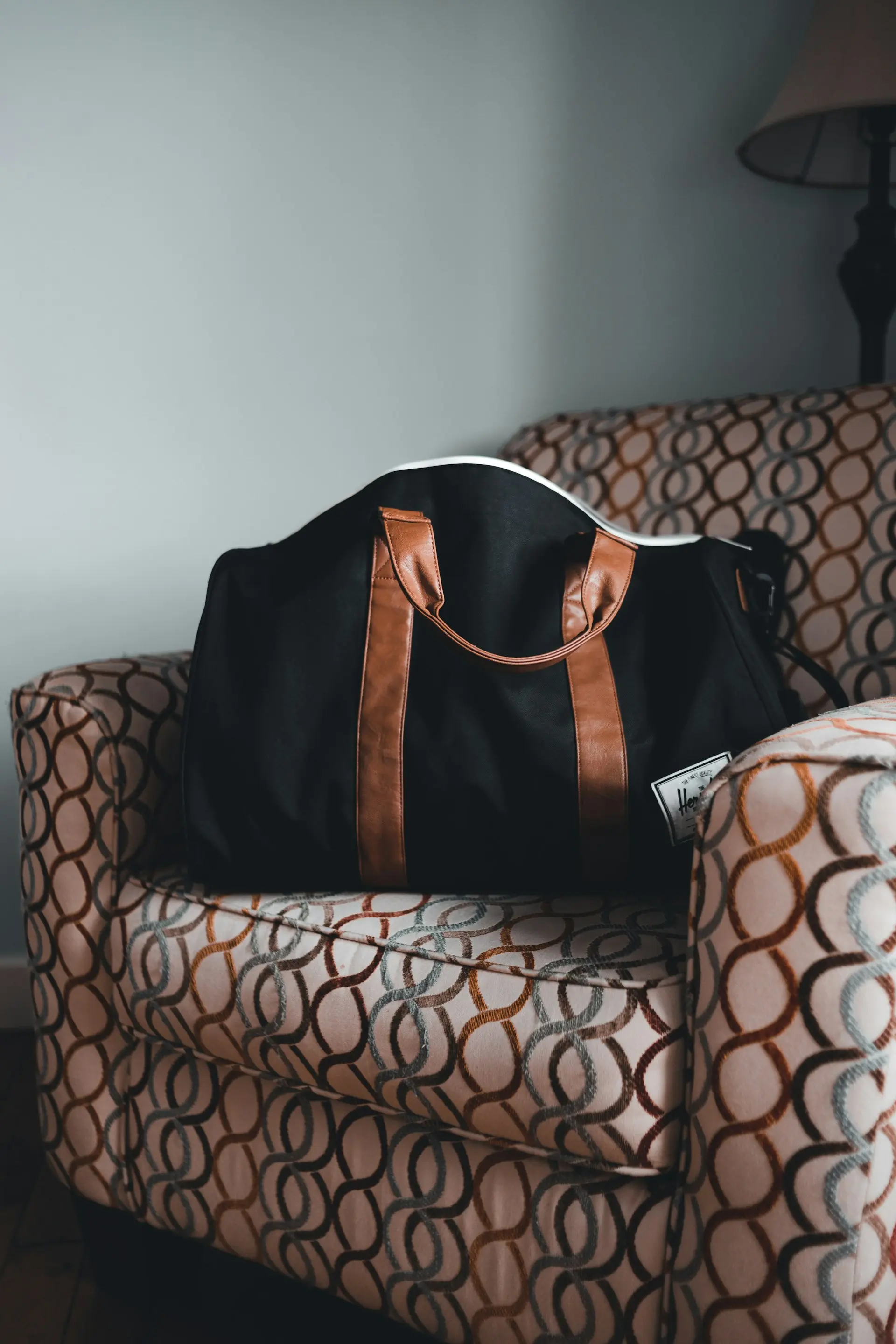 A black canvas holdall with tan leather handles on an armchair.