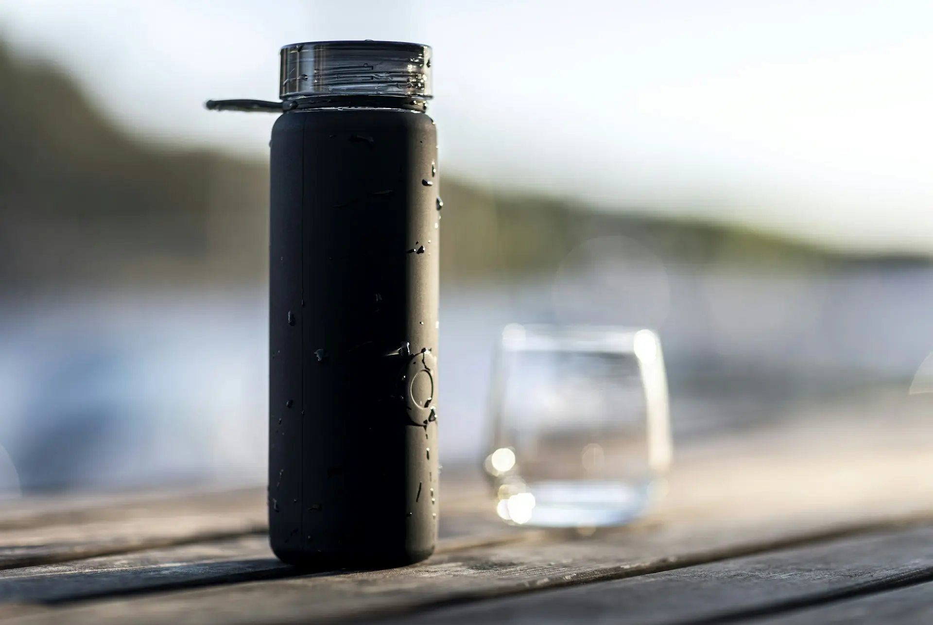 A matte black steel bottle beaded with water on warm wood.
