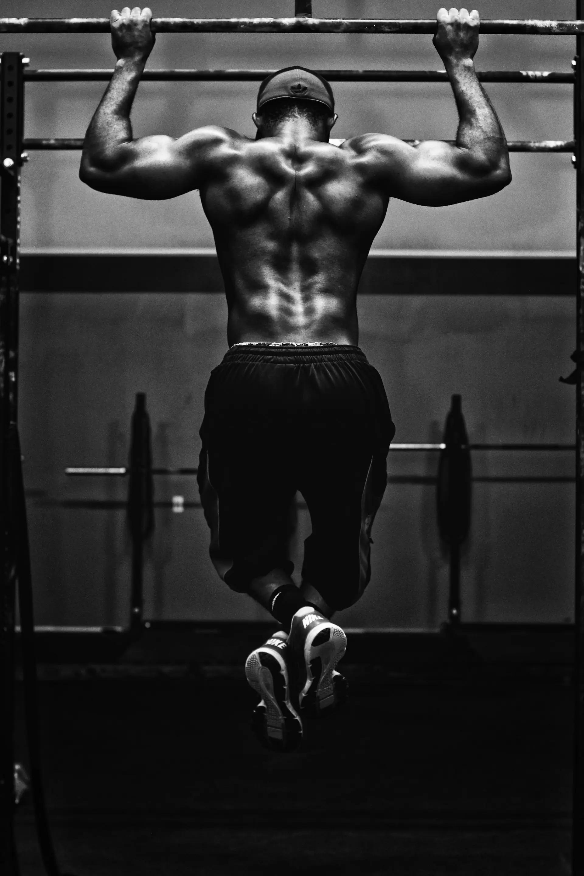 An athlete mid pull-up, back to the camera, lit hard against a dark gym.
