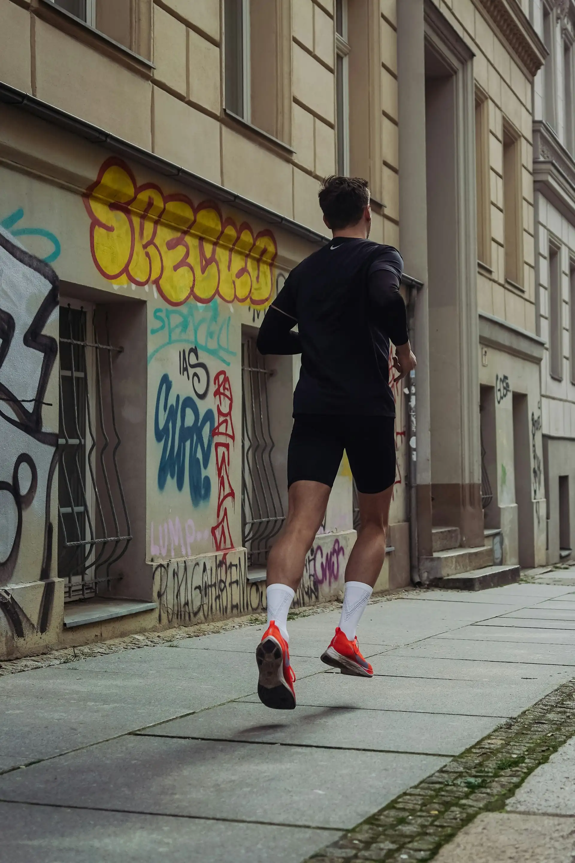 A man jogging in black shorts on a sidewalk.