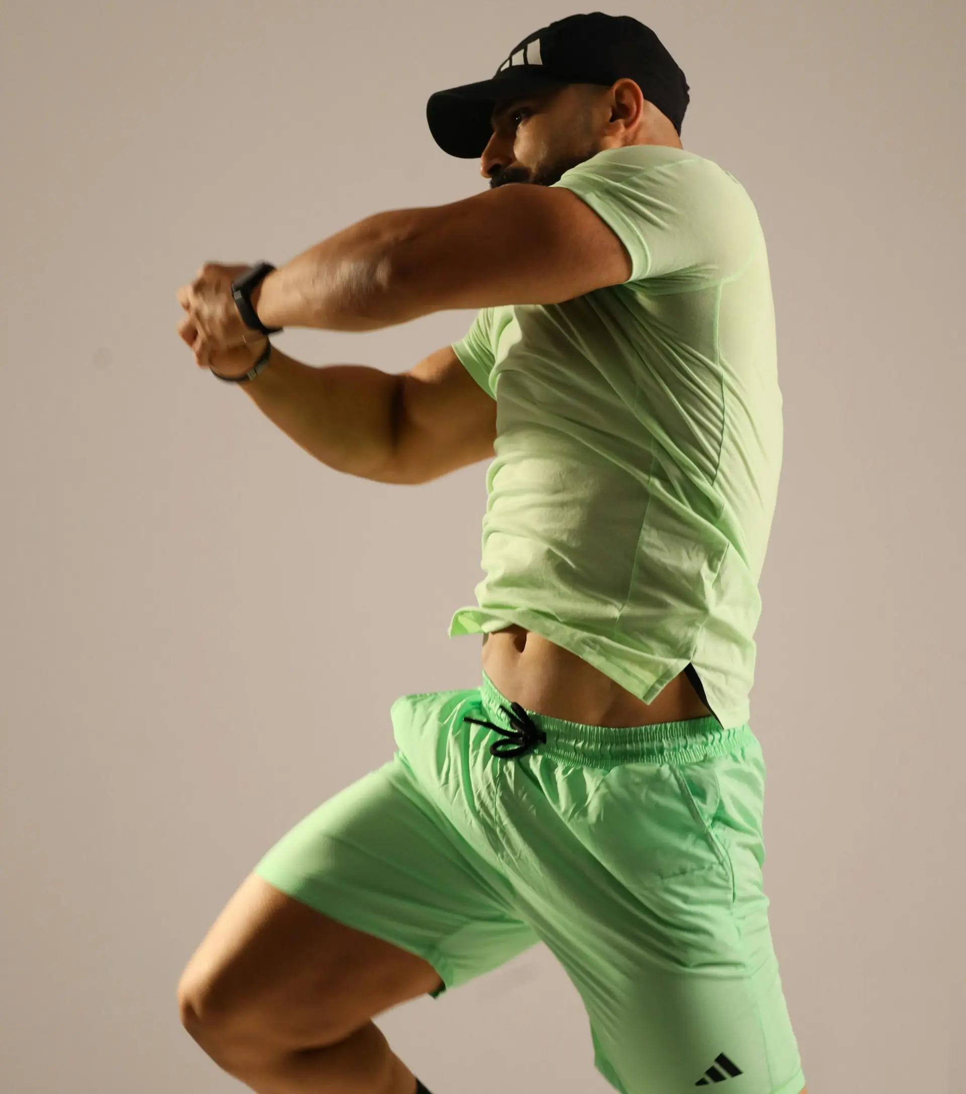 A man in a green shirt and shorts holding a racquet.