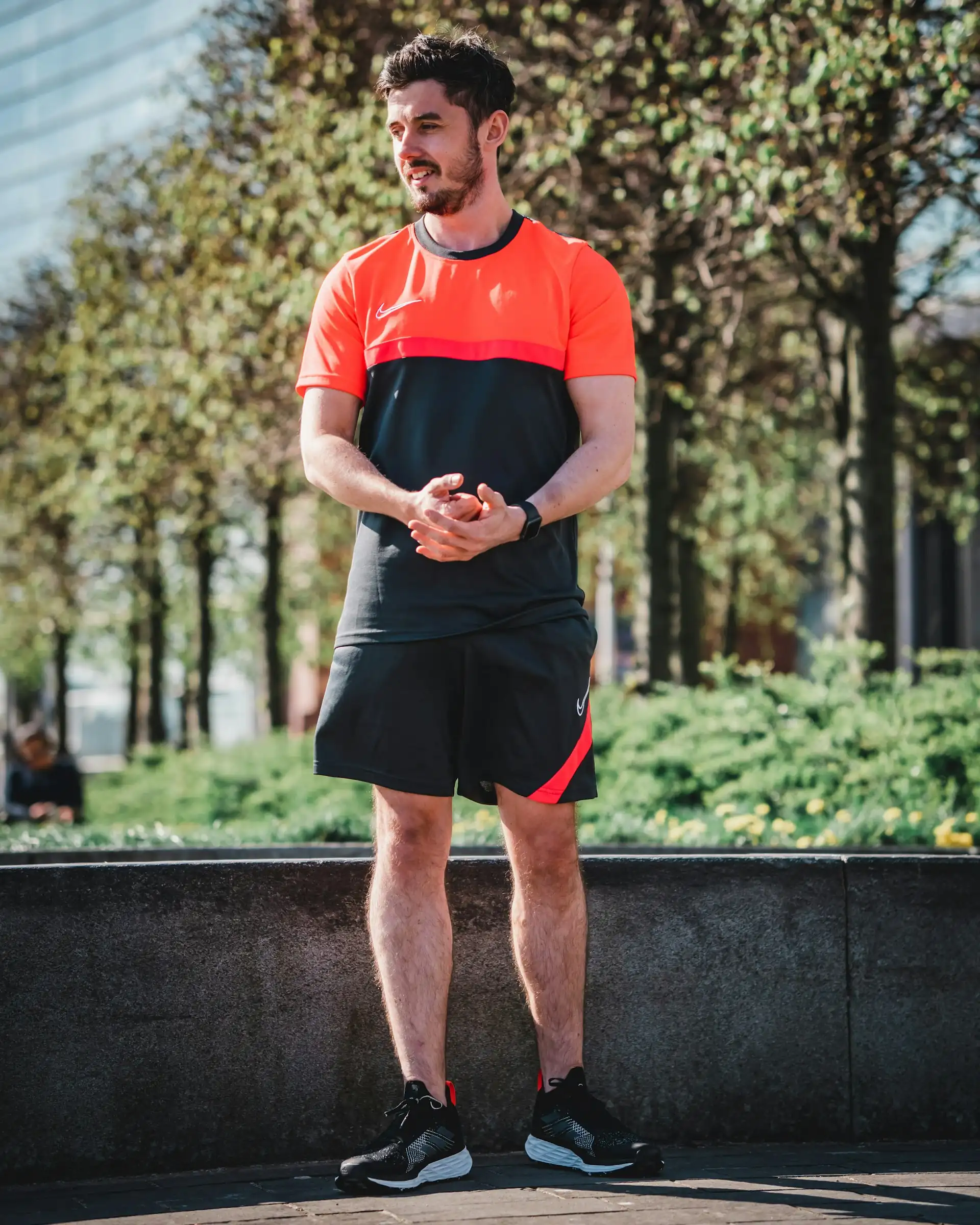 A man in a red tee and black shorts on grey paving.