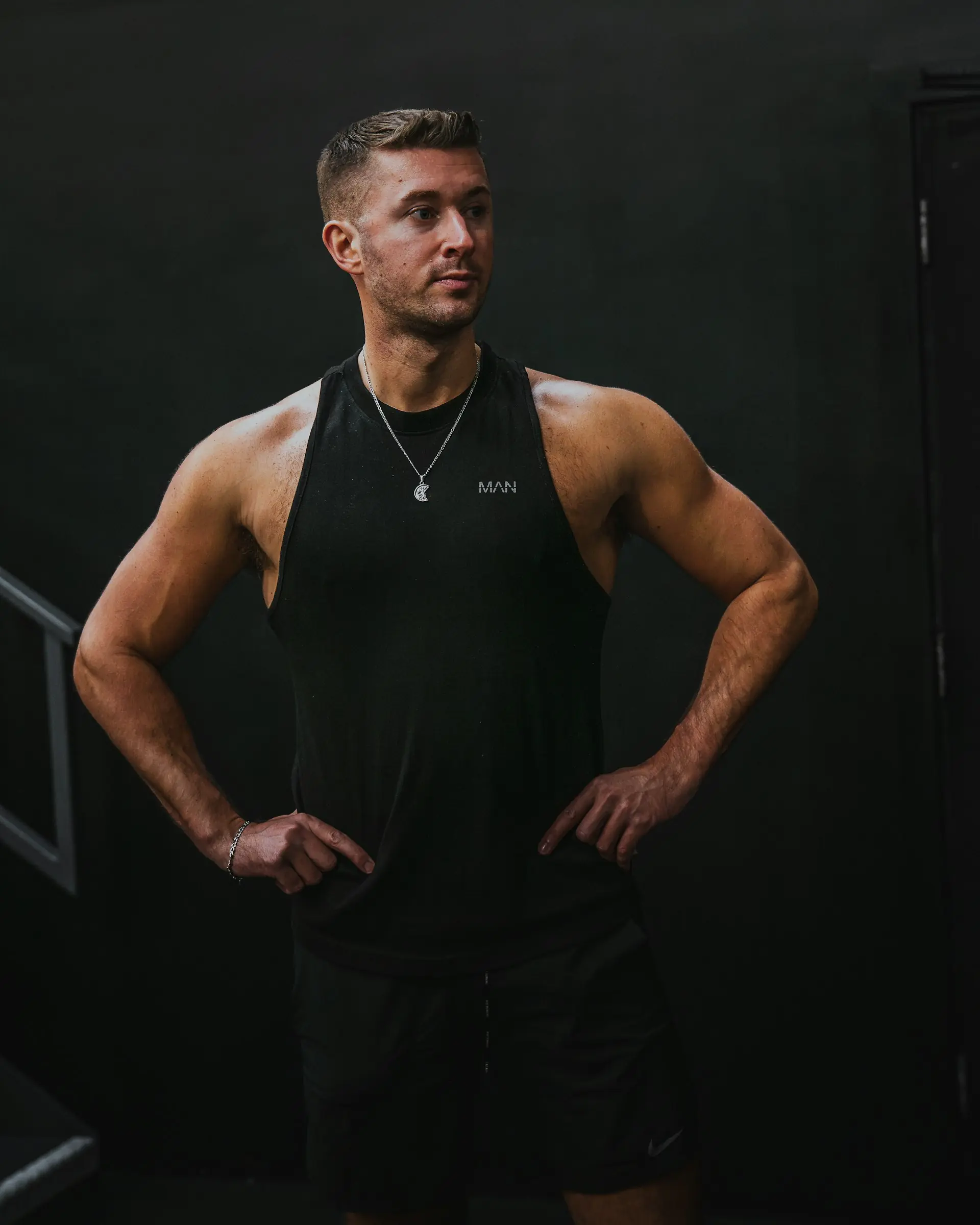 A man in a black tank, hands on hips.