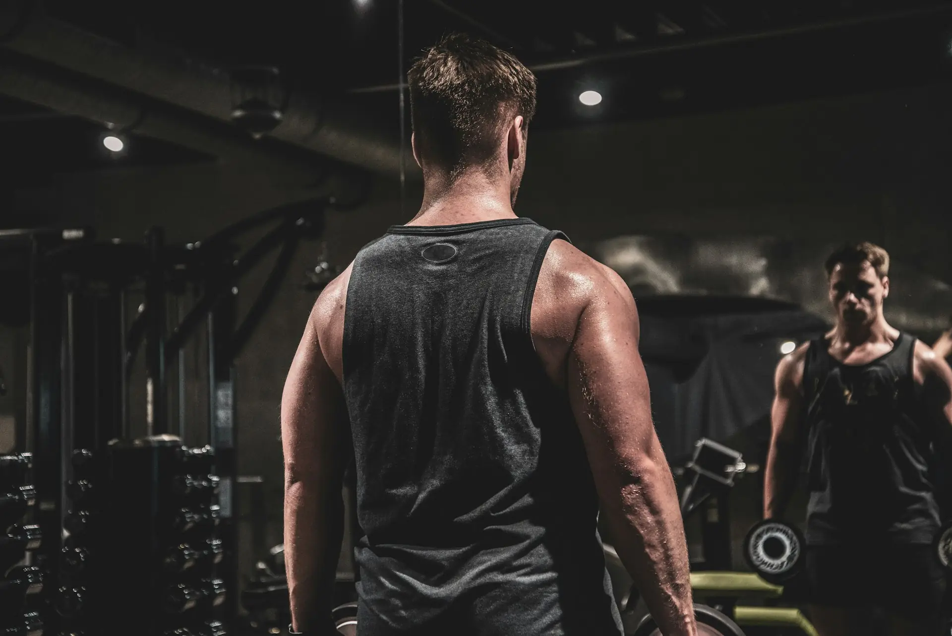 A man in a grey tank mid-set in the gym.