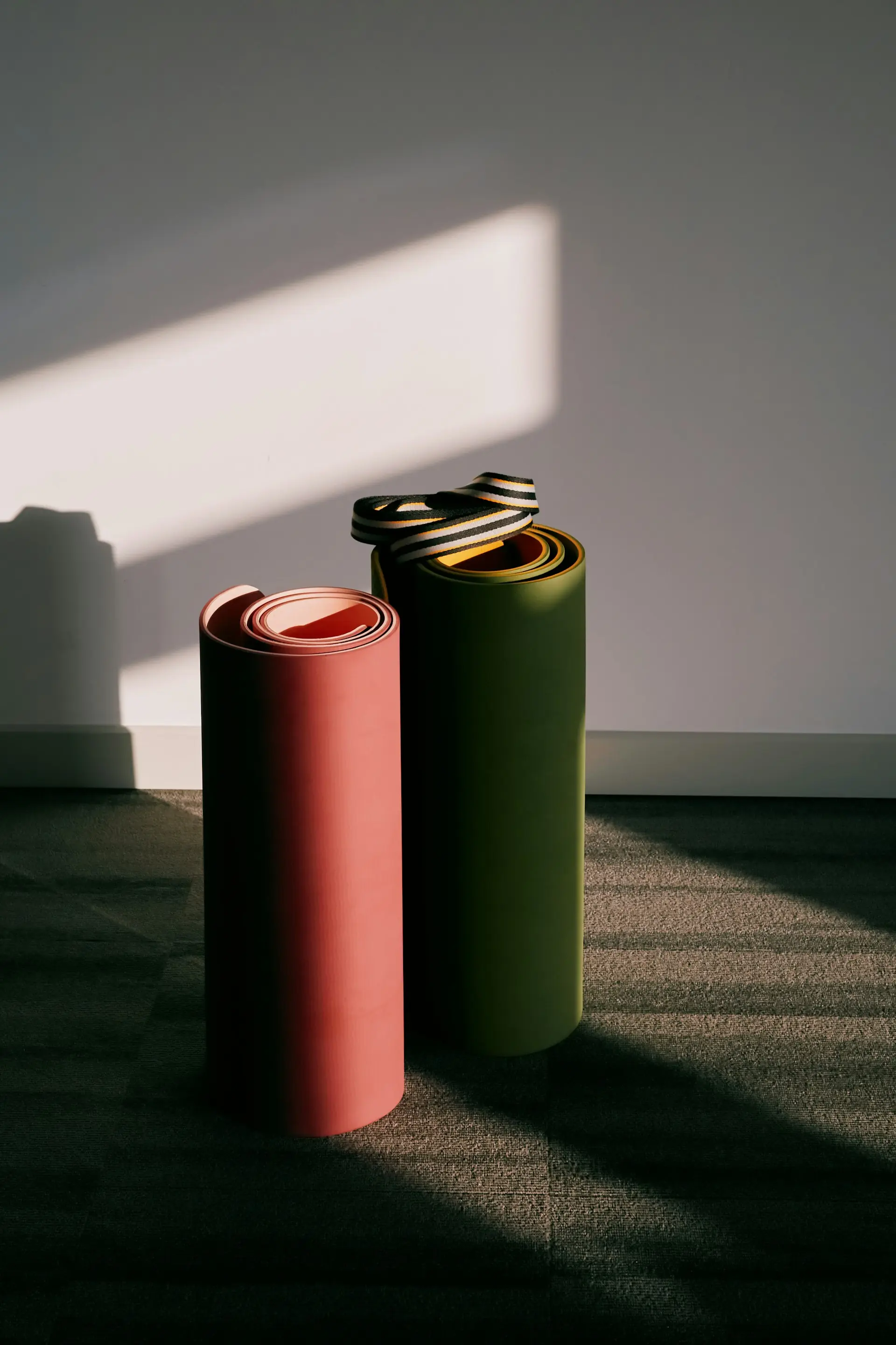 Two rolled training mats, terracotta and olive, standing in raking light.
