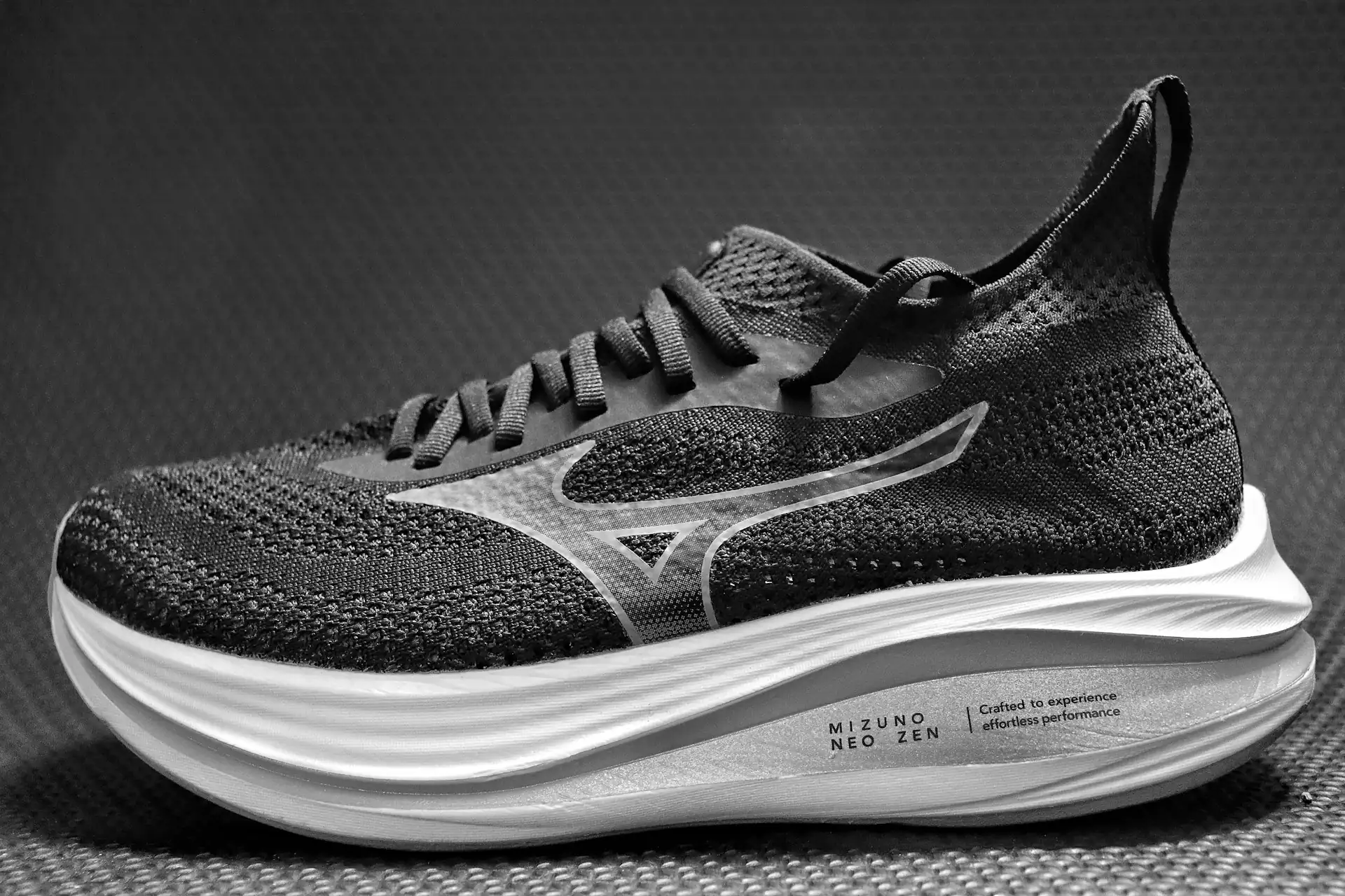 A road running shoe up close, black and white, on a dark ground.