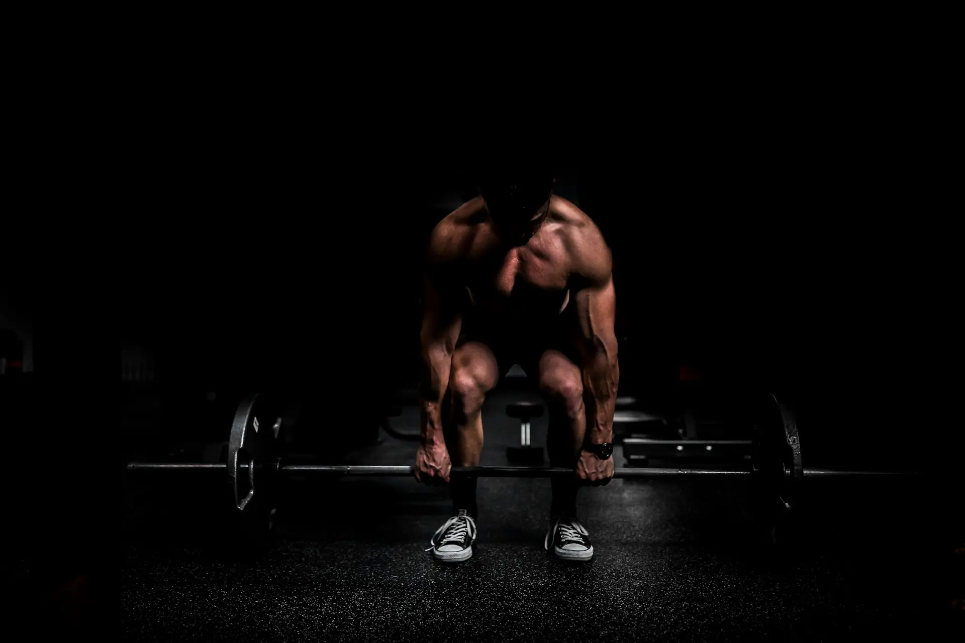 A lifter crouched over a barbell in near darkness.
