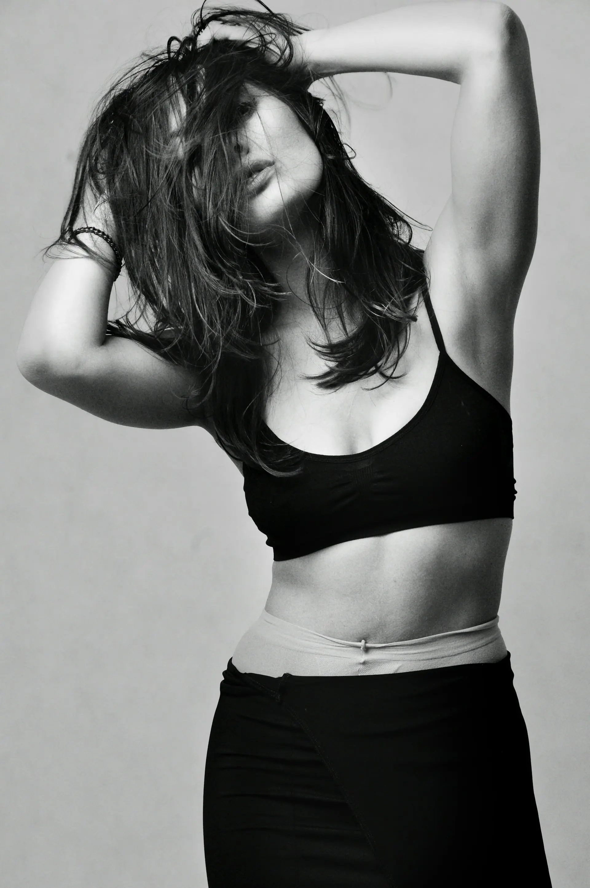 A woman in a black training top, hands in her hair.