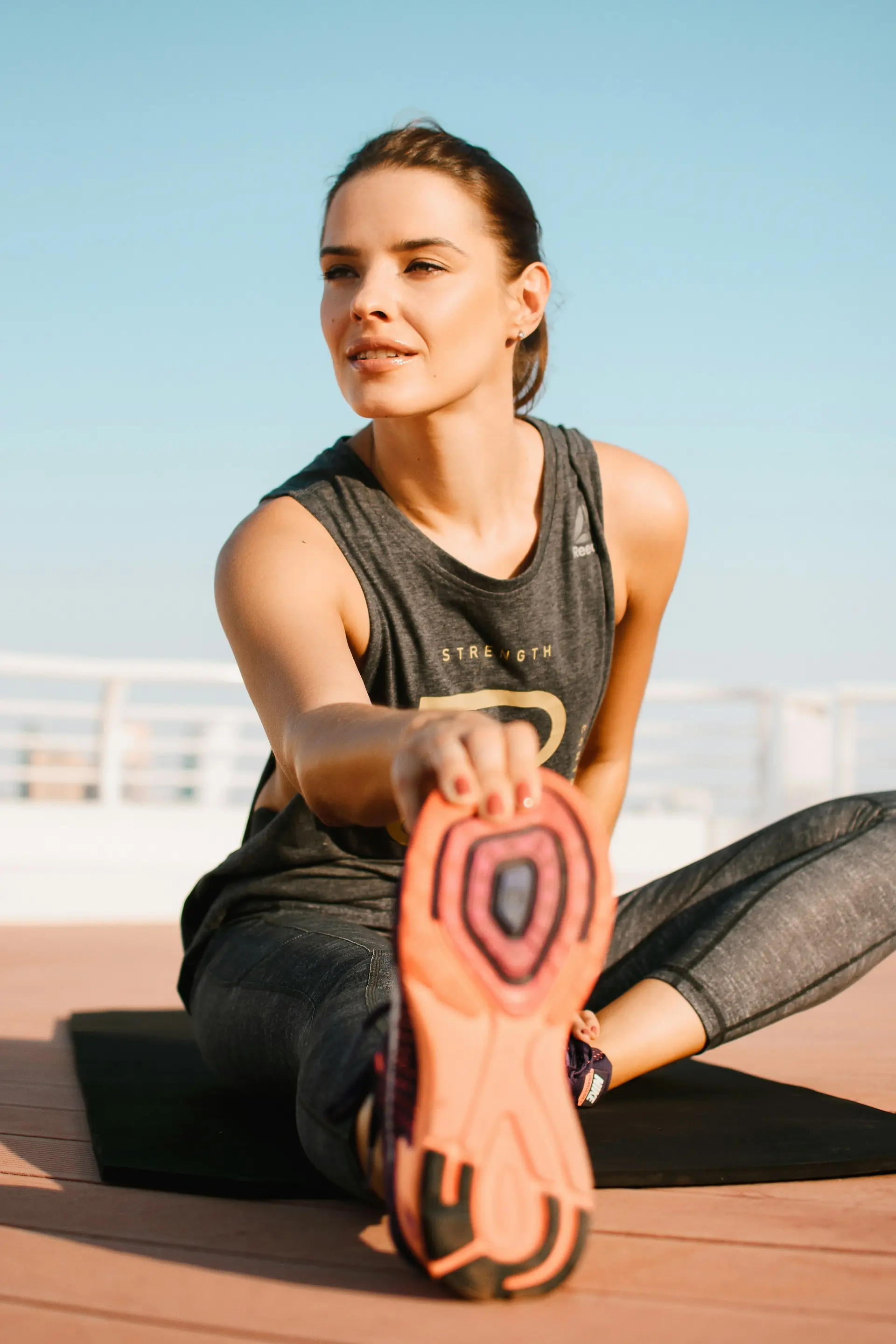 A woman in a grey tank stretching on a mat.