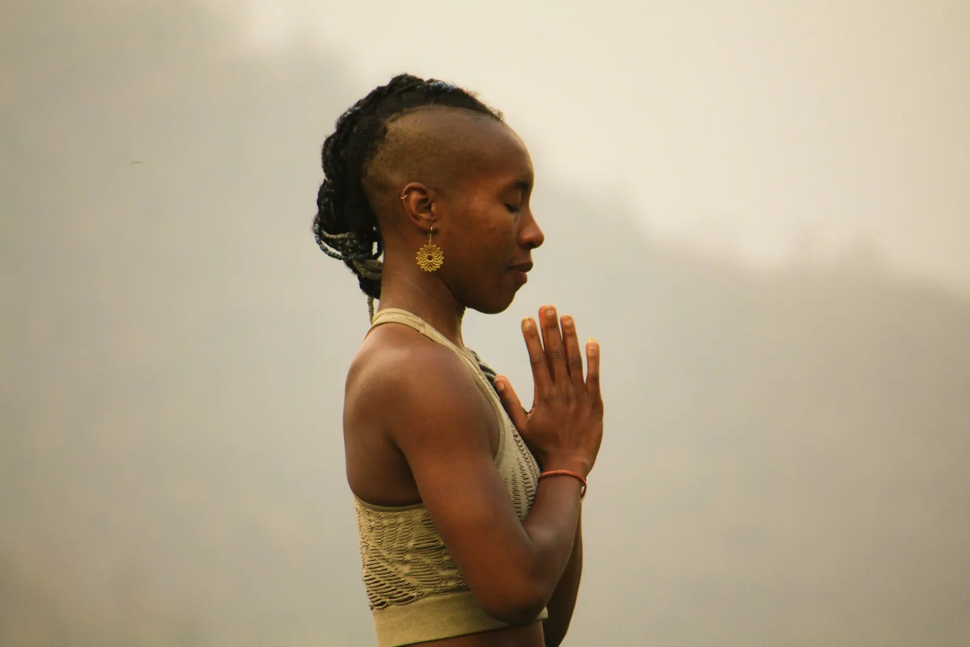 A woman in profile, palms together, in warm morning mist.