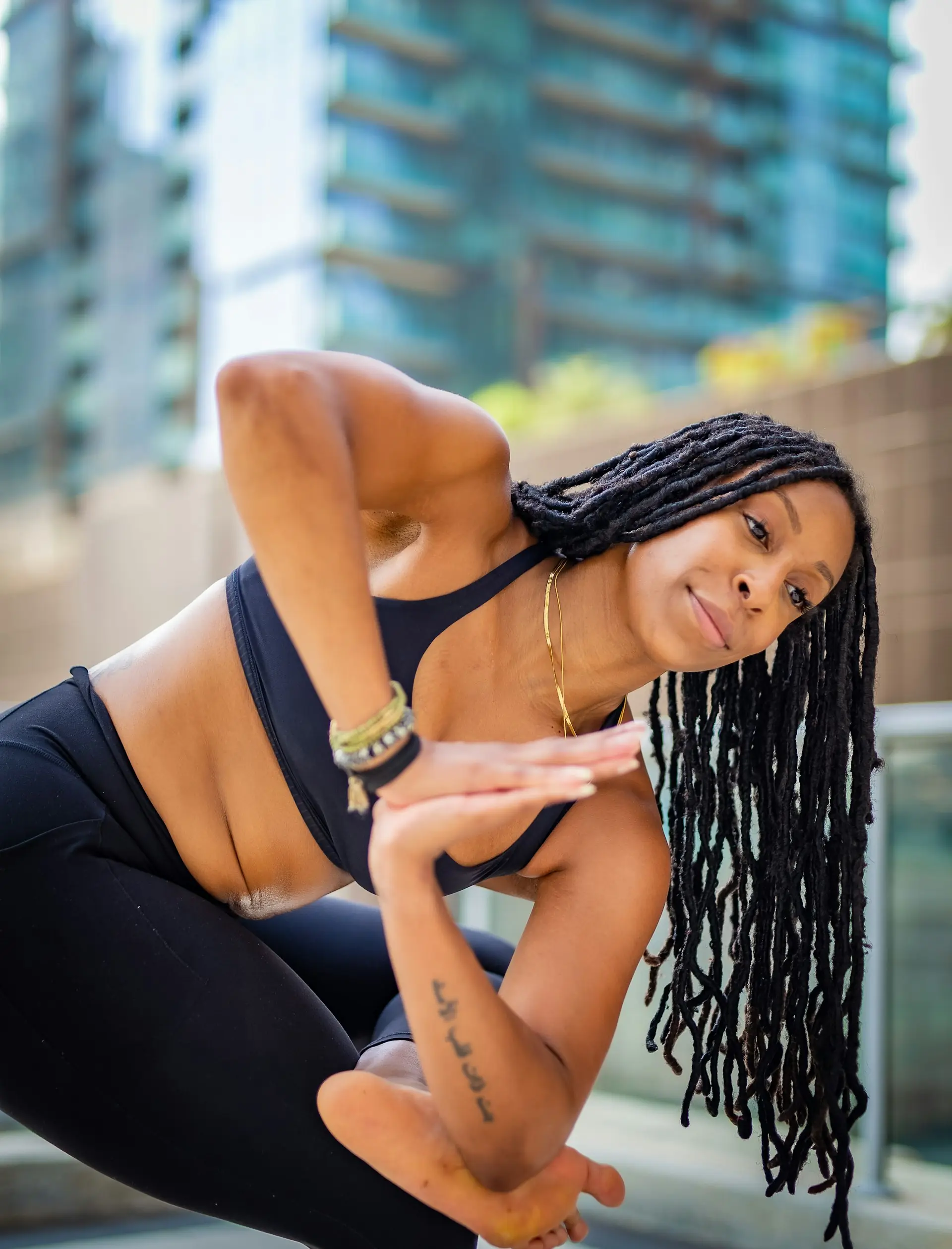 A woman with locs folded into a deep twist against the city.
